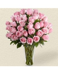 florero de cristal con rosas color rosado y follajes verdes 